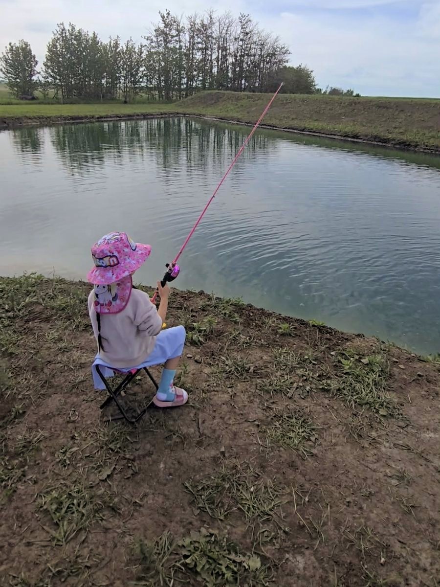 A girl in a sun hat fishing from a camp chair on the bank